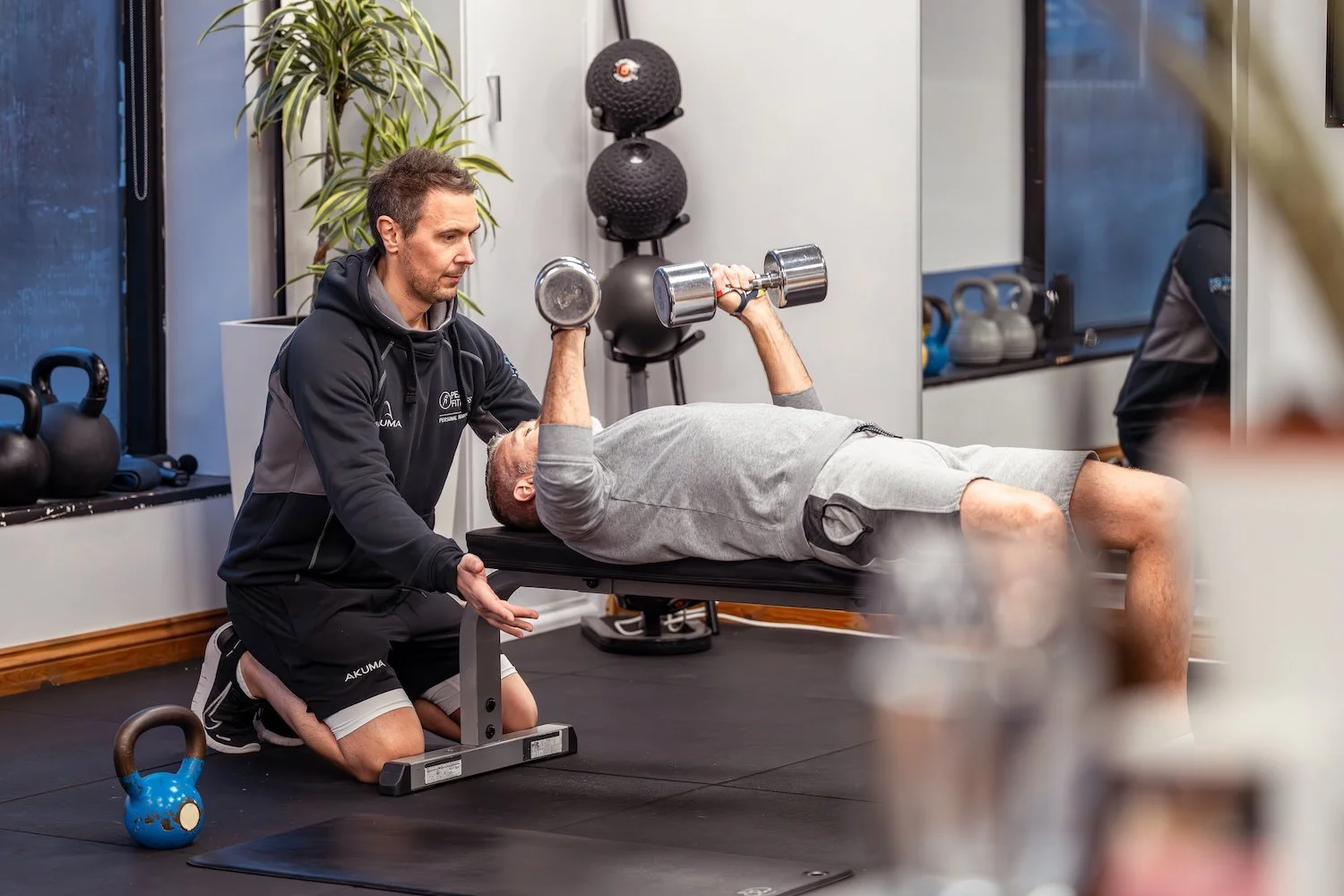 A personal trainer guiding a client through a dumbbell chest press at Peak Fitness Warwick